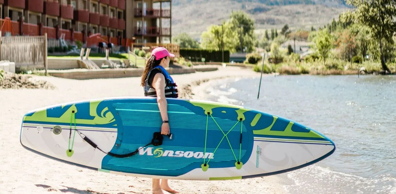 Guest carrying a paddleboard along the hotel beach